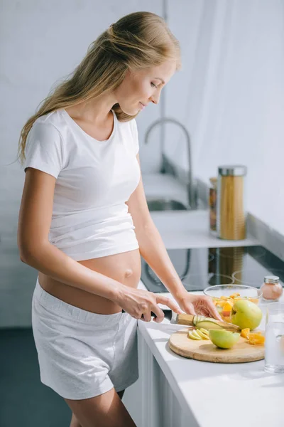 Vista Lateral Mulher Grávida Com Faca Cozinhar Salada Frutas Casa — Fotografia de Stock