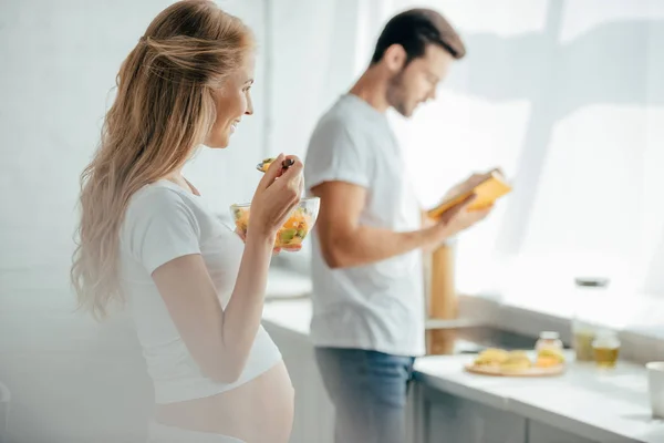 Selective Focus Pregnant Woman Eating Fruits Salad While Husband Book — Stock Photo, Image