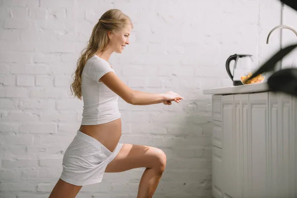 自宅でフィットネス練習をしている笑顔の妊娠中の女性の側面図 — ストック写真
