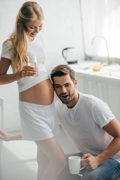 Hombre Con Taza Café Escuchando Vientre Esposa Embarazada Cocina Casa — Foto de Stock