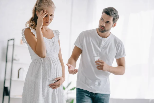 Zwangere Vrouw Witte Nachtjapon Met Hoofdpijn Terwijl Echtgenoot Geneesmiddelen Glas — Stockfoto