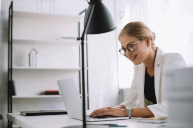 dizüstü bilgisayarda office işyerinde çalışan gülümseyen iş kadını yan görünüm