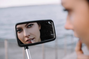 reflection of attractive young woman in mirror of motorcycle, selective focus