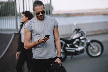 adam kız arkadaşı ile klasik motosiklet üzerinde arka plan ayakta iken smartphone kullanarak güneş gözlüğü