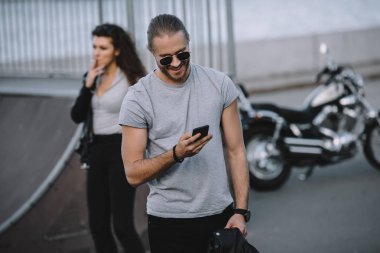 klasik motosiklet ile arka plan üzerinde duran kız iken Smartphone kullanan adam 