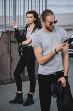 erkek kız arkadaşı ile klasik motosiklet üzerinde arka plan ayakta iken Smartphone kullanarak