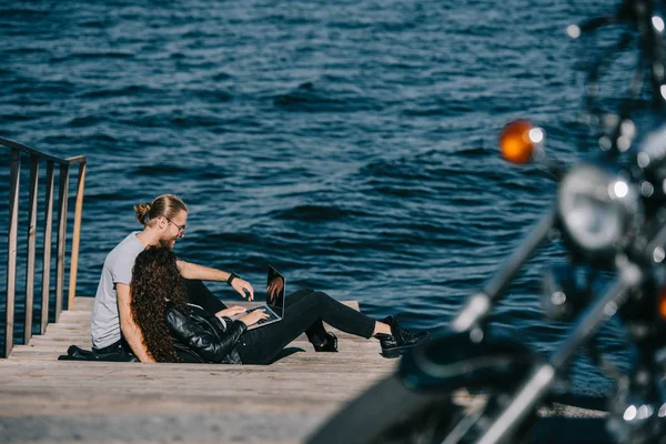夫妇使用笔记本电脑 而休息在码头附近的海边 有选择的重点摩托车 — 图库照片