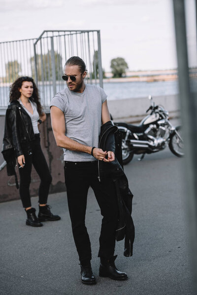 man and girlfriend in black leather jackets standing with classical motorbike 