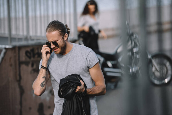 мужчина разговаривает по смартфону, пока девушка стоит с классическим мотоциклом
 