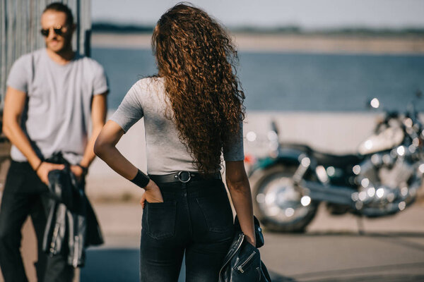 back view of woman going to man with classical motorbike 