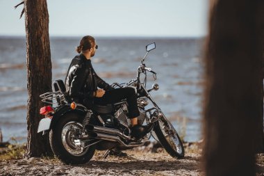 Motorcu deri ceketli klasik motosiklet deniz kenarında oturup...