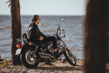 biker in leather jacket sitting on classical motorbike near the sea clipart
