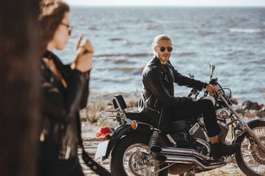 selective focus of man sitting on motorcycle while his girlfriend smoking on foreground clipart