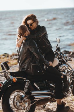 couple in black leather jackets hugging on vintage motorbike on seashore clipart