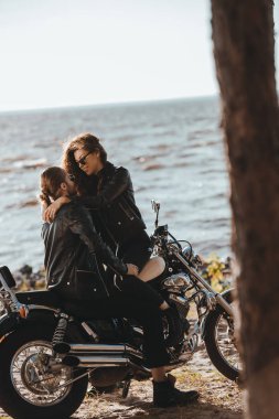 Genç bir çift deniz kıyısı üzerinde klasik motosiklet üzerinde kucaklayan