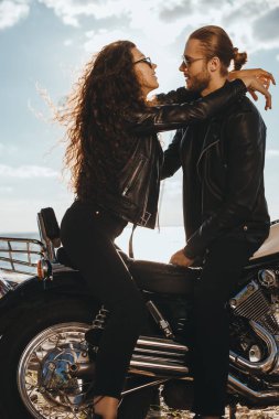 couple of bikers in black leather jackets hugging on chopper motorcycle clipart