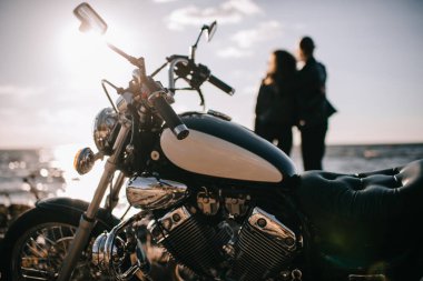 selective focus of classical chopper motorbike and couple looking at sea on background clipart