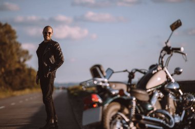 smiling man standing on road with classical motorcycle, selective focus clipart