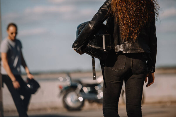 back view of girlfriend holding helmet and going to boyfriend with classical motorbike 