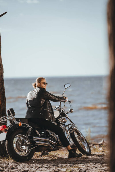 biker in black leather jacket sitting on chopper motorcycle near the sea