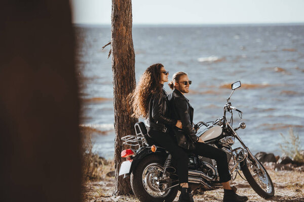 couple in black leather jackets sitting on classical chopper motorbike on seashore