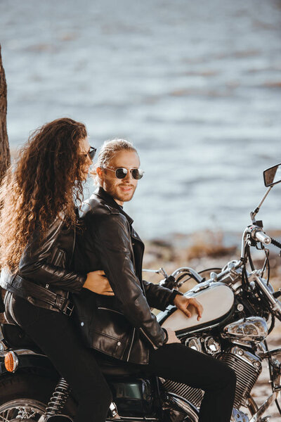 пара байкеров в черных кожаных куртках, сидящих на мотоцикле на берегу моря
