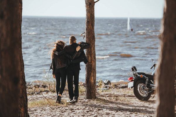 rear view of couple of bikers hugging and looking at sea, motorbike standing near
