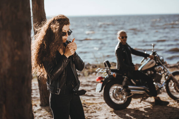 selective focus of girlfriend smoking cigarette while boyfriend sitting on motorbike on seashore