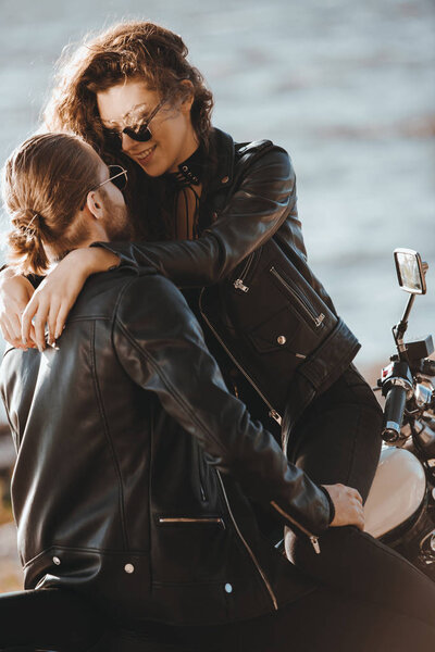 couple of bikers in black leather jackets hugging on motorcycle on seashore