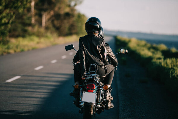 rear view of couple in helmets riding chopper motorbike on country road