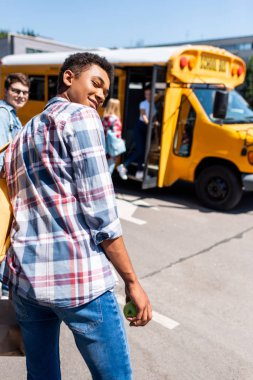 okul otobüsü sınıf arkadaşları ile yürüme ve geri dönüş kameraya genç Afro-Amerikan okul çocuğu dikiz