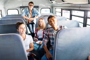 group of happy teen scholars riding school bus and looking at camera clipart