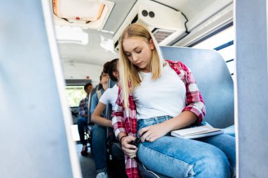 teen schoolgirl riding school bus with classmates and fastening seat belt  clipart