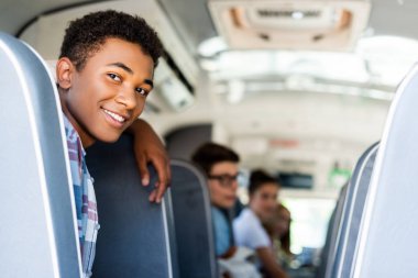 teen students sitting at school bus and looking back at camera clipart