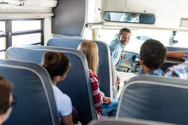 group of teen scholars riding school bus and talking with happy mature driver clipart