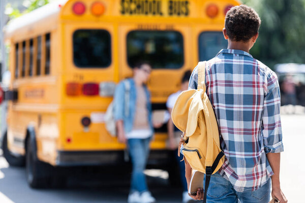 rear view of teen schoolboy walking to classmates leaning on school bus