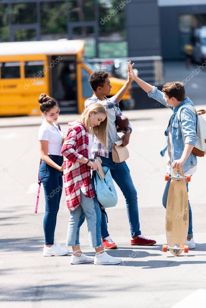 group of teen scholars giving high five on parking in front of school bus