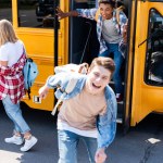 Grupo de jóvenes eruditos felices corriendo en la escuela desde el autobús