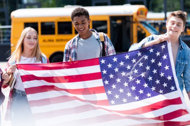 Grup Genç öğrenciler okul otobüsü önünde ABD bayrak tutan gülümseyerek