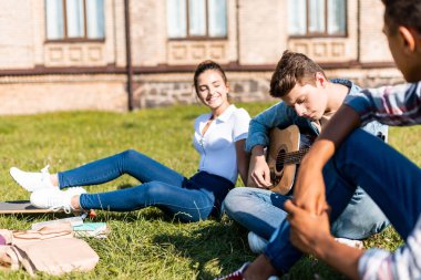 çimenlerin üzerinde oturan ve öğle yemeği sırasında akustik gitar çalmak mutlu genç grup