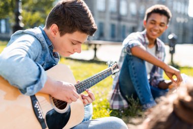 çimenlerin üzerinde oturan ve akustik gitar çalmak mutlu gençler