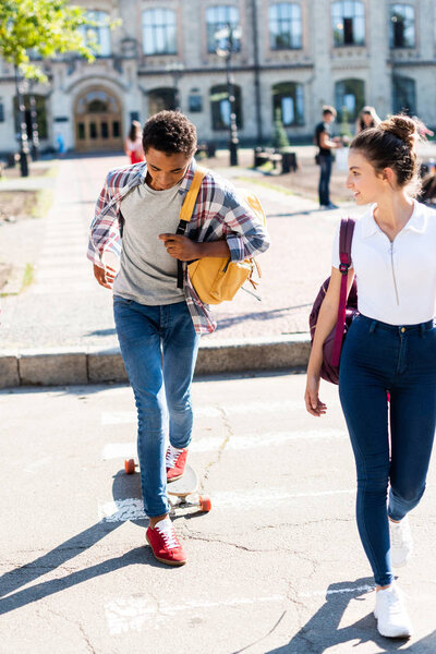 teen students walking at college garden with skateboard