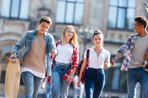group of happy multiethnic teenagers with backpacks having walk together with old school building on background