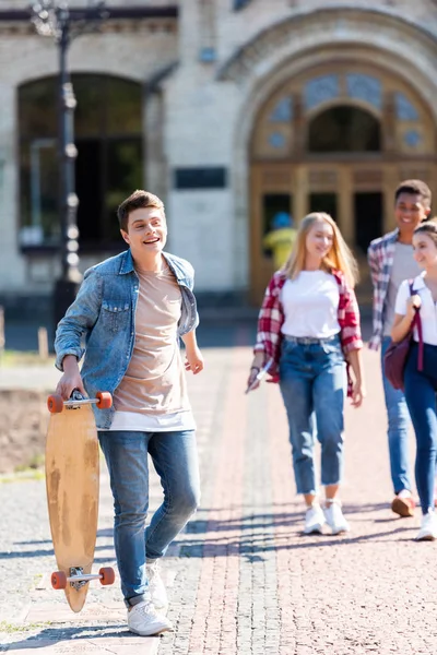 愉快的少年学生与滑板步行与朋友放学后 — 图库照片