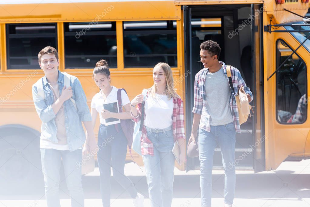 group of teen scholars walking together in front of school bus