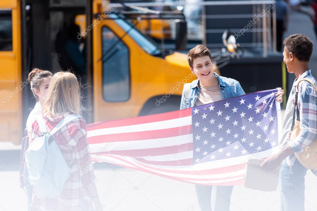 group of american teen scholars with united states flag in front of school bus