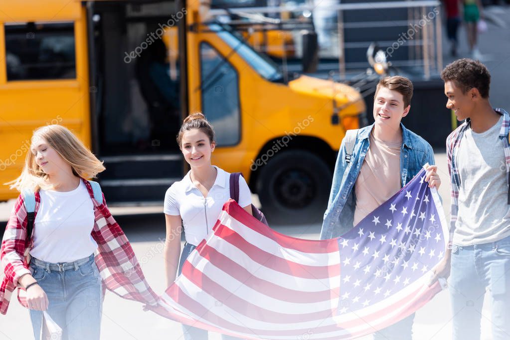 group of american teen scholars walking with usa flag in front of school bus