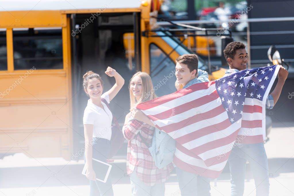 group of happy american teen scholars with usa flag in front of school bus