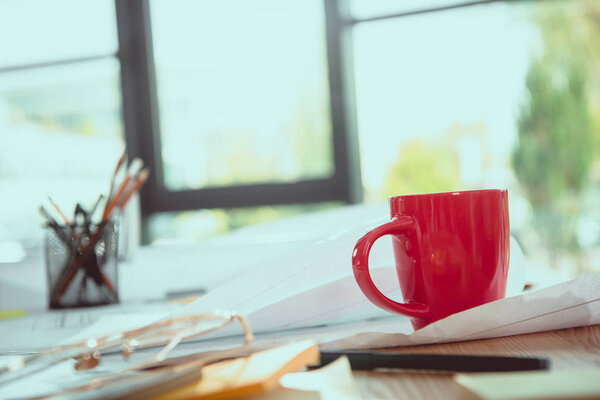 Close-up view of various office supplies, coffee cup and blueprints on office table