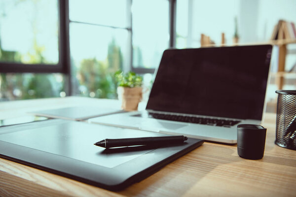 laptop with blank screen and graphics tablet on wooden tabletop at office